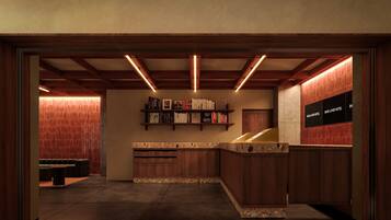 A modern hotel lobby with a wooden reception desk, a bookshelf with books, and a sign indicating the hotel name.