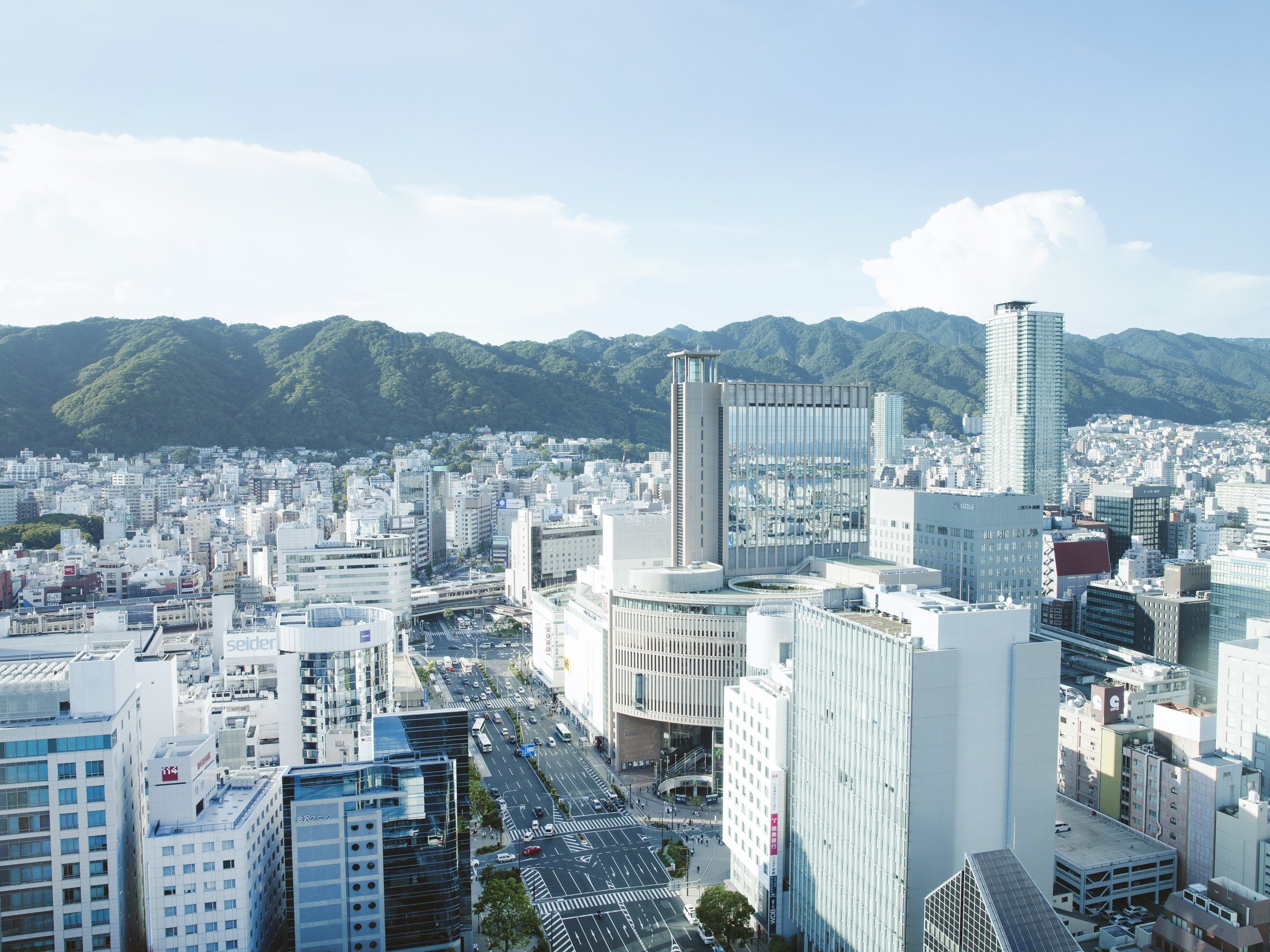 Paisagem urbana com edifícios modernos, uma via central e uma cordilheira ao fundo.