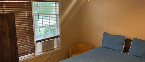 A bedroom with a bed, a window with blinds, a ceiling fan, and a small stool.