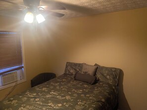 A bedroom with a bed, a ceiling fan, a window with blinds, and a wall-mounted heater. - Enchanting Guest Studio with backyard vibe (Conley)