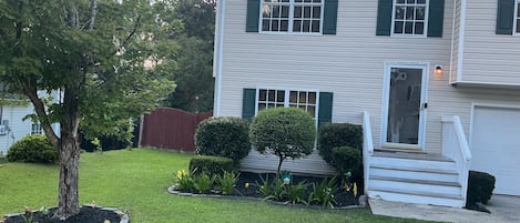 A two-story house with a front porch, a lawn, and a red fence.