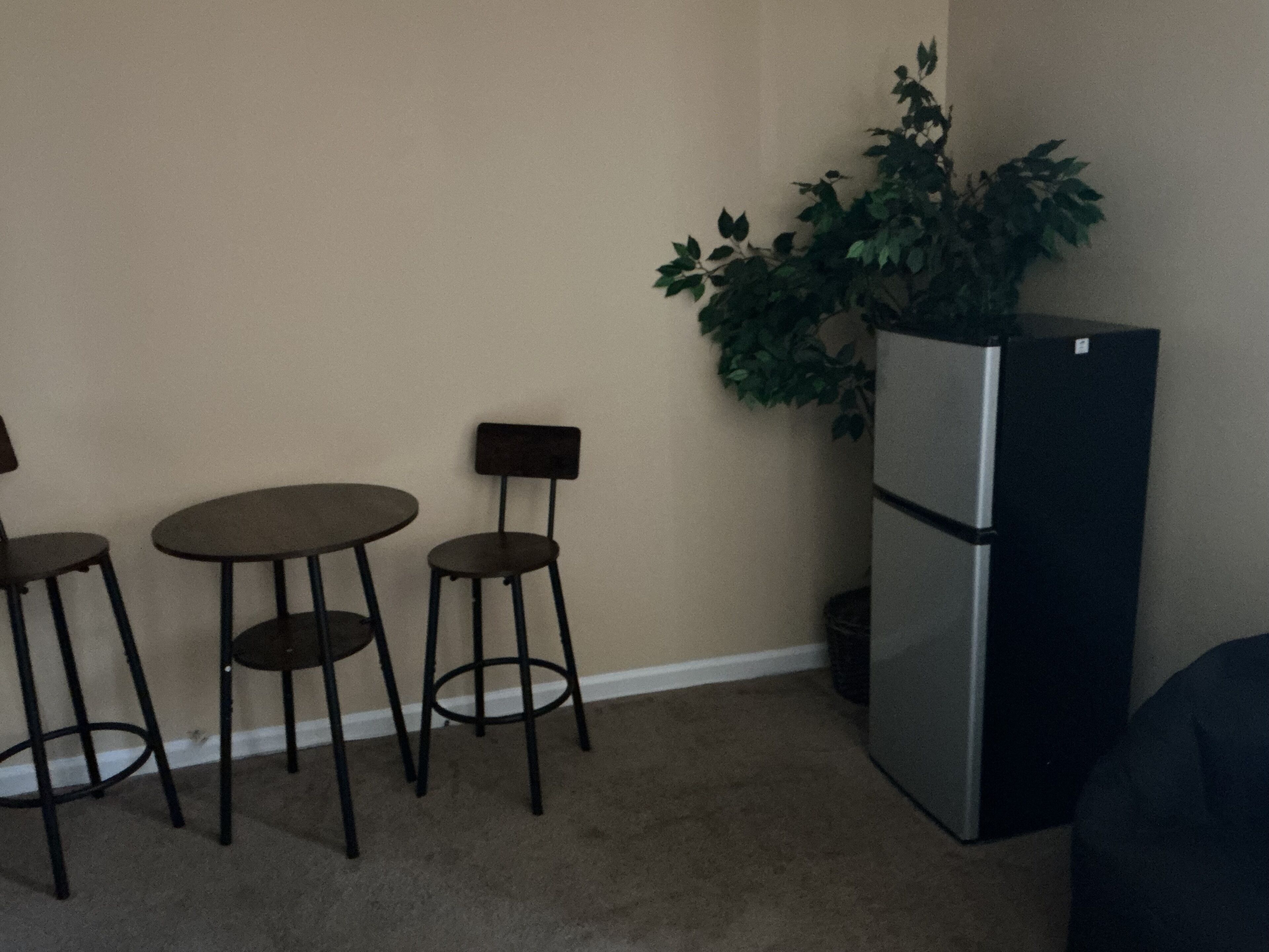 Une petite cuisine équipée d’un réfrigérateur, de deux tabourets de bar et d’une plante en pot.