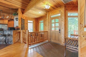 Ein Holzblockbau-Innenraum mit Kamin aus Stein, einer Holztreppe und Blick ins Freie.