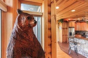 Ein rustikaler Innenraum mit einer Holzskulptur eines Bären, einer Steinwand und einer Küchenzeile mit Holdekor und einem Barhocker.