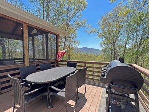 Une terrasse avec une table et des chaises, un barbecue et une vue sur les arbres et les montagnes.