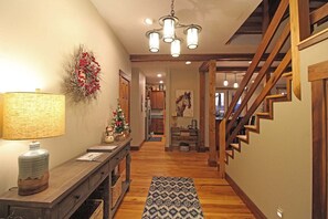 A wooden staircase leading to a second floor, a dining area with a table and chairs, and a kitchen in the background. - Haven in the Woods- Luxury Rental in the Heart of Bryson City, NC (Bryson City)