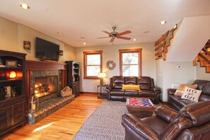 A cozy living room with a fireplace, leather sofas, a coffee table, and a staircase. - Haven in the Woods- Luxury Rental in the Heart of Bryson City, NC (Bryson City)