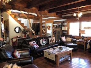 Ein gemütliches Wohnzimmer mit Kamin, Ledersofas, einem Holztisch und einer Treppe, die in ein Obergeschoss führt.