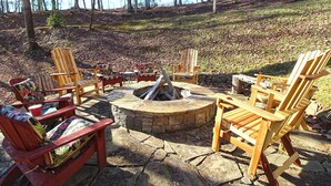 Et udendørs opholdsområde med Adirondack-stole og en pejseplads i sten.