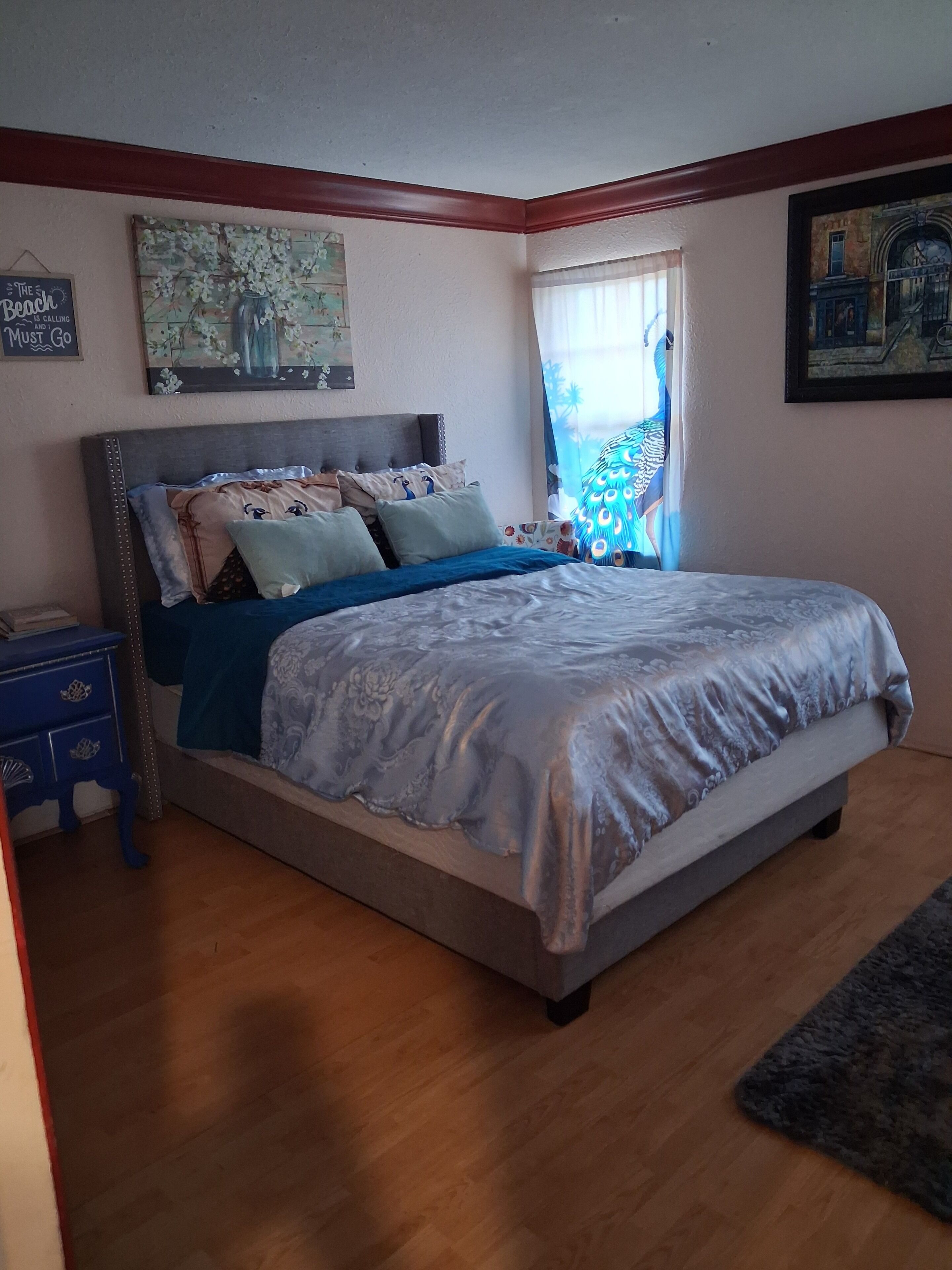A bedroom with a bed, a nightstand, a dresser, and a window with curtains.