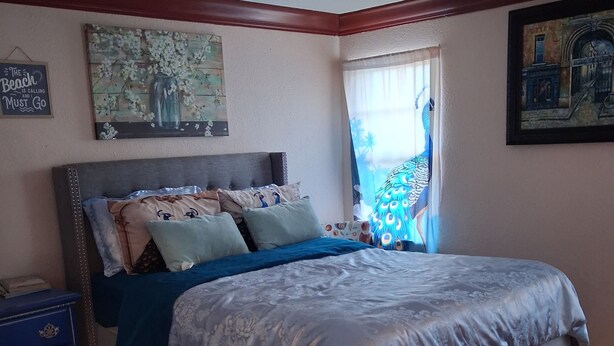 Um quarto com cama, mesa de cabeceira, cômoda e janela com cortinas.