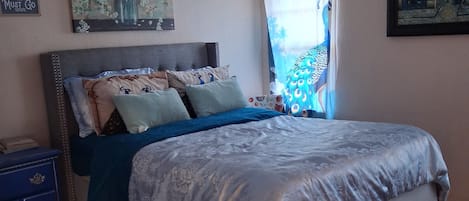 A bedroom with a bed, a nightstand, a dresser, and a window with curtains.