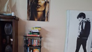 Una sala de estar con un sofá azul oscuro, una estantería con varios objetos y dos obras de arte enmarcadas en la pared.