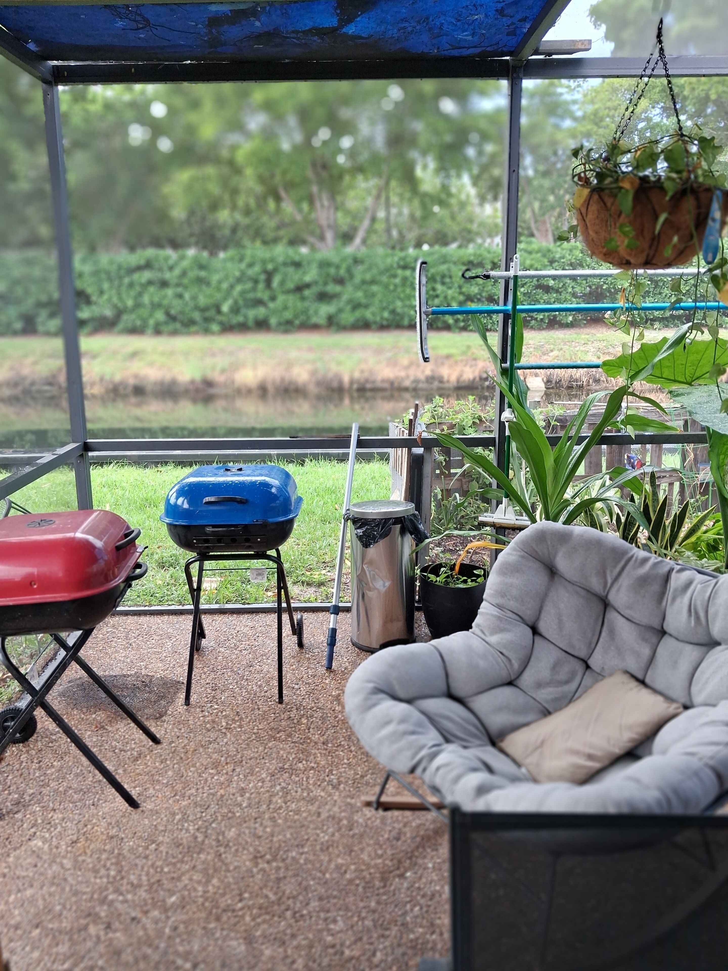 Un espace extérieur abrité, équipé d’un barbecue, d’une chaise et de plantes suspendues.