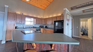 A kitchen with wooden cabinets, a black refrigerator, and a central island with stools. - On Top of the World- Amazing Views (Bryson City)