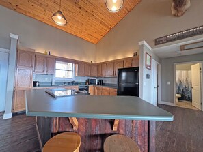 A kitchen with wooden cabinets, a black refrigerator, and a central island with stools. - On Top of the World- Amazing Views (Bryson City)