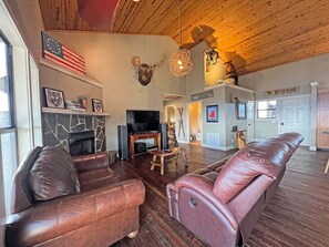 Ein geräumiges Wohnzimmer mit Ledersofas, einem Steinkamin, einer aufgehängten amerikanischen Flagge und einem Fernseher.
