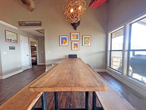 A spacious room with a long wooden table, framed artwork on the walls, and large windows. - On Top of the World- Amazing Views (Bryson City)