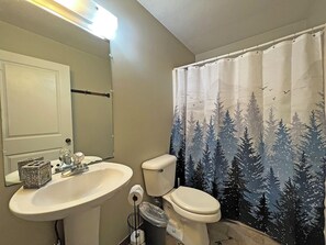 Un baño con lavamanos, inodoro y cortina de ducha con estampado de bosque.