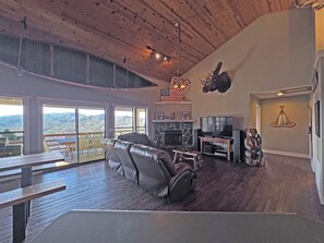 A spacious living room with a fireplace, a mounted moose head, and a large window overlooking a mountainous landscape. - On Top of the World- Amazing Views (Bryson City)