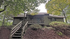 A rustic cabin with a wooden staircase leading up to a porch, surrounded by dense foliage. - On Top of the World- Amazing Views (Bryson City)