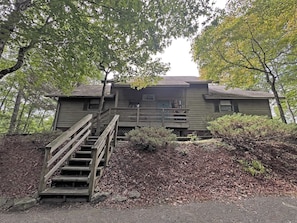 A rustic cabin with a wooden staircase leading up to a porch, surrounded by dense foliage. - On Top of the World- Amazing Views (Bryson City)