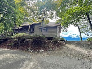 Un chalet rustique doté d’un porche, entouré d’arbres et accessible par un chemin de gravier.