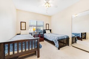 Ein Schlafzimmer mit zwei Betten, einem Schreibtisch, einem Stuhl, einem Deckenventilator und einem großen Spiegel.