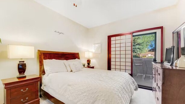 A bedroom with a bed, bedside tables, a dresser, a TV, and a sliding glass door leading to an outdoor area. - Prime location deluxe condo with pool and hot tub in beautiful Phoenix (Phoenix)
