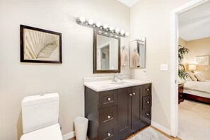 A bathroom with a white toilet, dark brown vanity with drawers, a large mirror with lights, and a framed botanical print on the wall. - Prime location deluxe condo with pool and hot tub in beautiful Phoenix (Phoenix)