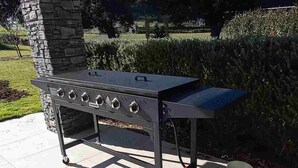 Un barbecue installé à l’extérieur, avec un pilier en pierre, une bouteille de gaz et un ciel dégagé en arrière-plan.