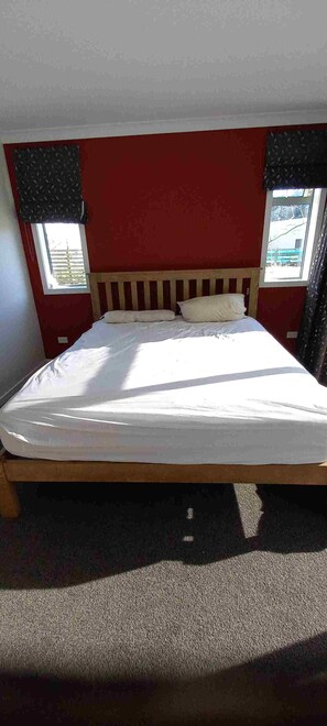 Une chambre avec un lit simple, une tête de lit en bois, une fenêtre avec vue et un sol recouvert de moquette.