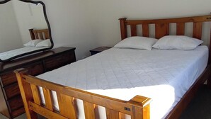 Un lit simple avec un cadre en bois et une literie blanche, dans une pièce dont le sol est recouvert d’une moquette.