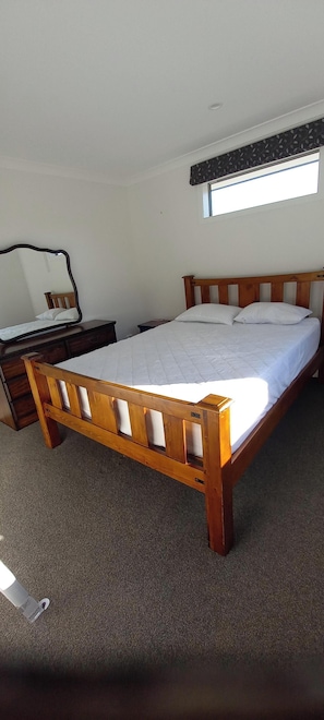 Ein Einzelbett mit Holzrahmen und weißer Bettwäsche in einem Zimmer mit Teppichboden.