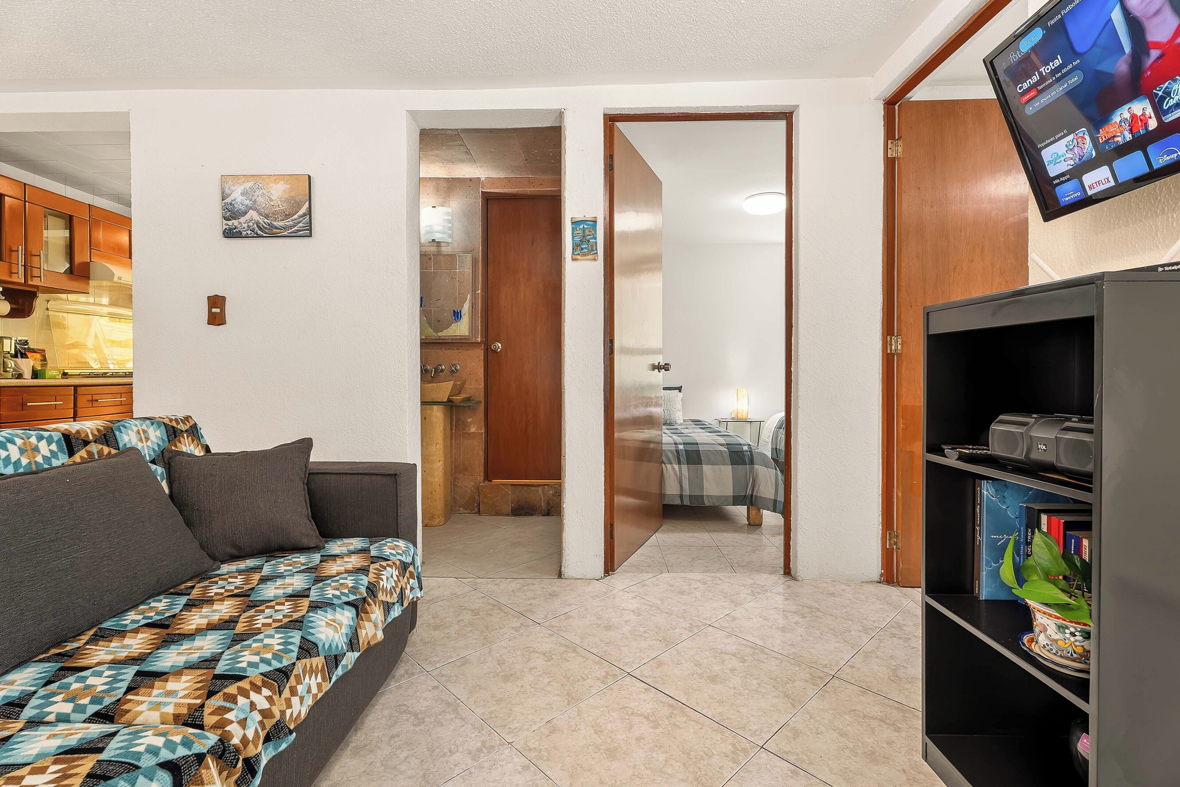 Un espacio habitable compacto con sofá, televisor montado en la pared y estantería.
