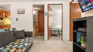Un espacio habitable compacto con sofá, televisor montado en la pared y estantería.