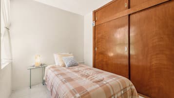 A bedroom with a bed, bedside table, lamp, and a wooden wardrobe.