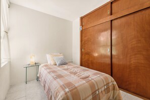 A bedroom with a bed, bedside table, lamp, and a wooden wardrobe.