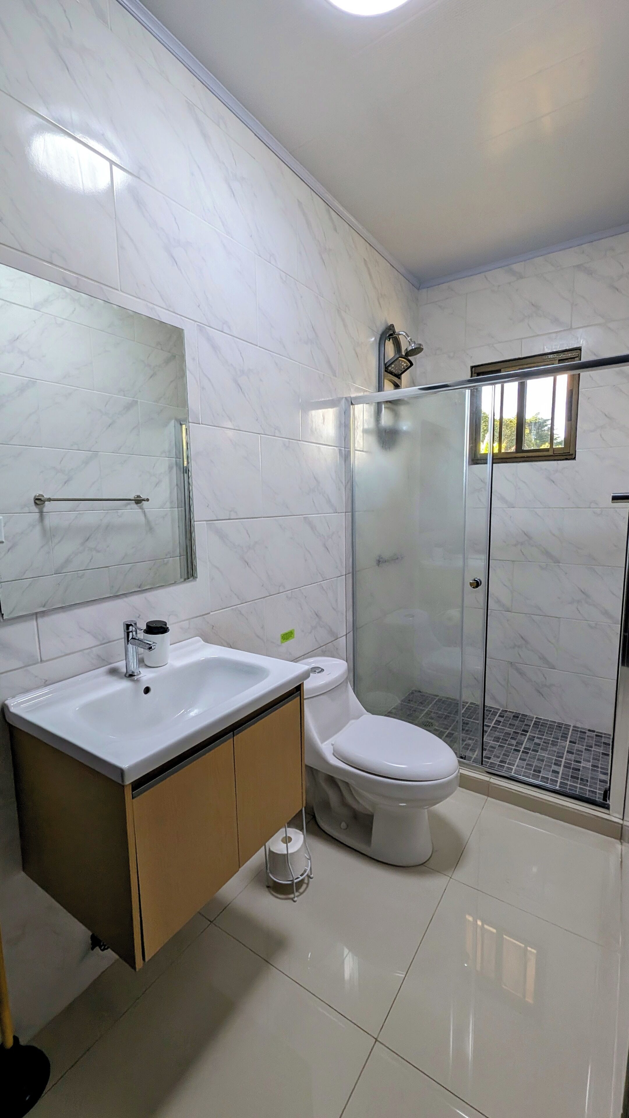 A modern bathroom with a marble floor, a glass shower enclosure, a white sink, and a toilet.