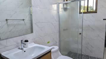 A modern bathroom with a marble floor, a glass shower enclosure, a white sink, and a toilet.