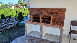 An outdoor brick oven barbecue area with a stone wall and a chair.
