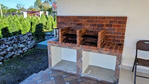 An outdoor brick oven barbecue area with a stone wall and a chair.