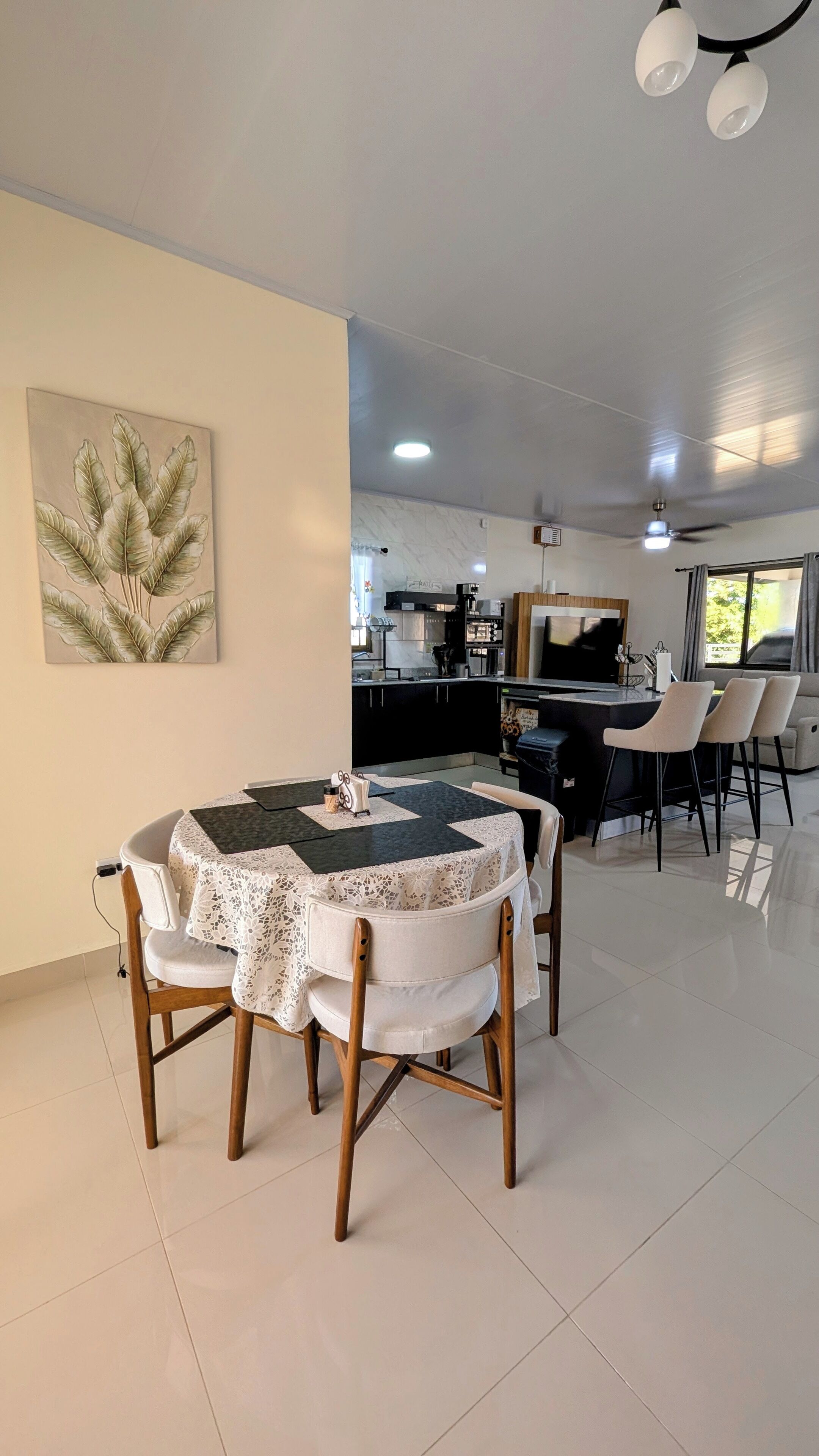 A dining area with a table and chairs, a kitchen in the background, and a ceiling fan.
