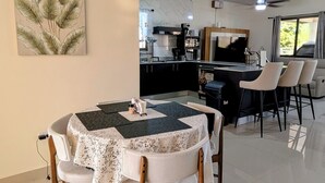 A dining area with a table and chairs, a kitchen in the background, and a ceiling fan.
