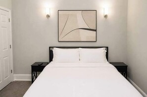 Ein Schlafzimmer mit einem Bett, zwei Nachttischen, einem an der Wand befestigten Kunstwerk und zwei Wandleuchten.