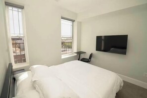 A bedroom with a bed, a flat-screen TV mounted on the wall, and two windows. - Central Station North Mega Apartment - Free (Baltimore)