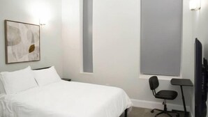 Una camera da letto con un letto, una sedia, una TV a schermo piatto e un'opera d'arte appesa al muro.
