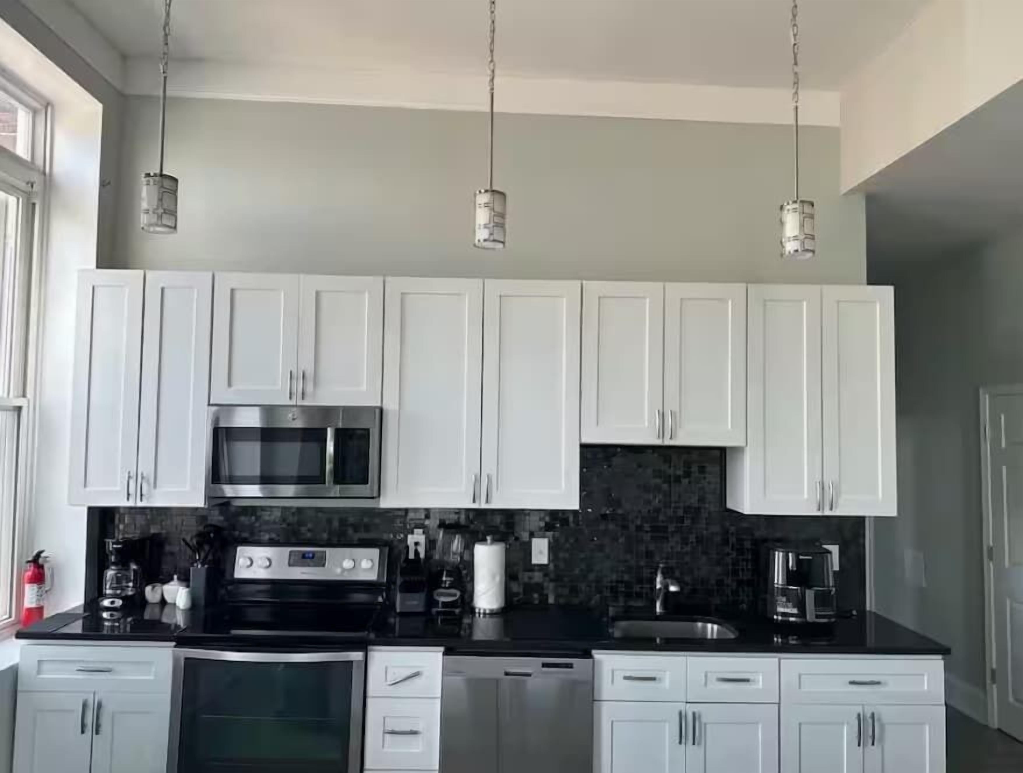 A modern kitchen with white cabinets, a black countertop, a microwave, and hanging pendant lights.