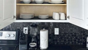 Una cucina con pensili aperti che espongono piatti bianchi e una macchina da caffè sul piano di lavoro.