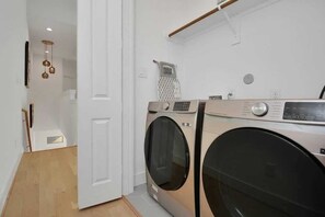 A laundry area with two front-loading washing machines, a white door, and a hanging light fixture. - Pet-Friendly Midtown House, Private Yard & BBQ (Houston)
